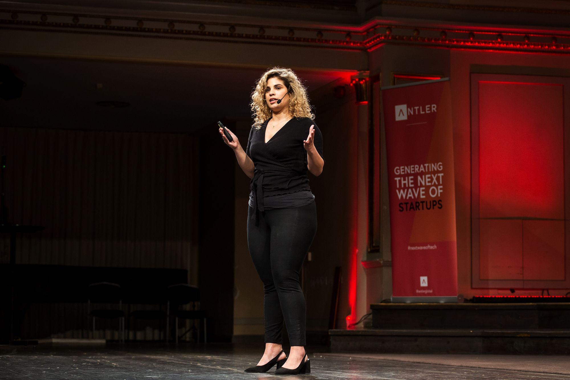 A founder pitching on stage at an Antler Demo Day, in front of a red Antler banner